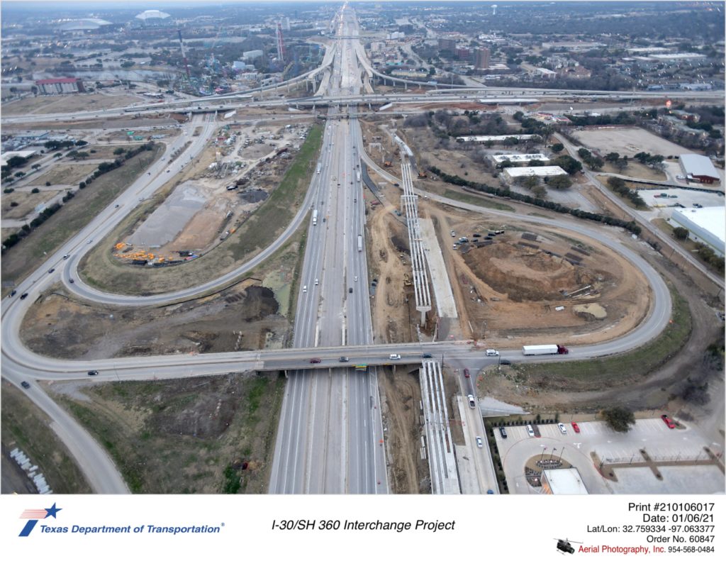Over I-30 looking west with Six Flags Dr interchange in foreground. Construction of new westbound direct connector ramp to north and south SH 360 shown being constructed, as well as new westbound frontage road west of Six Flags Dr intersection.
